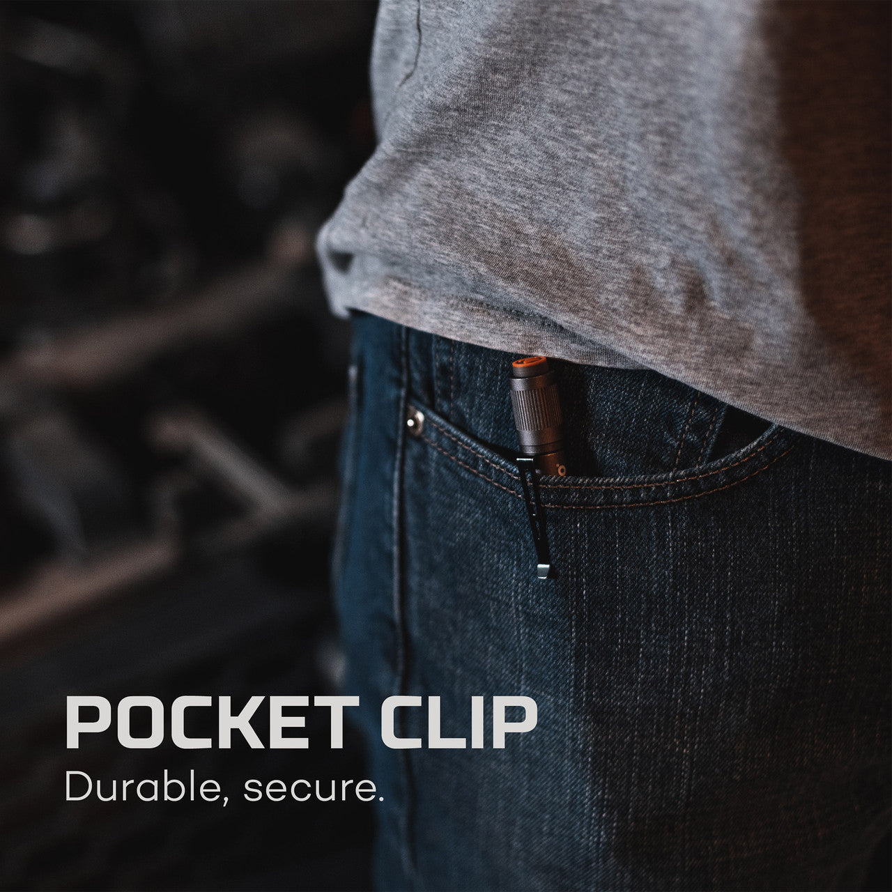 Pocket clip attached to the edge of a jeans pocket, partially visible beneath a gray shirt.