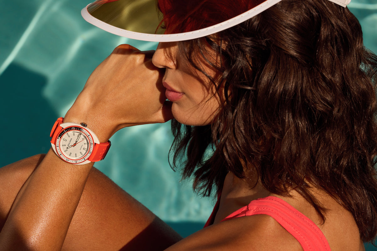 Woman wearing a Bulova Snorkel watch with an orange strap by the pool