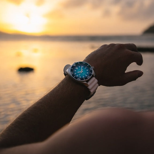 Wristwatch with a blue face against a sunset backdrop.