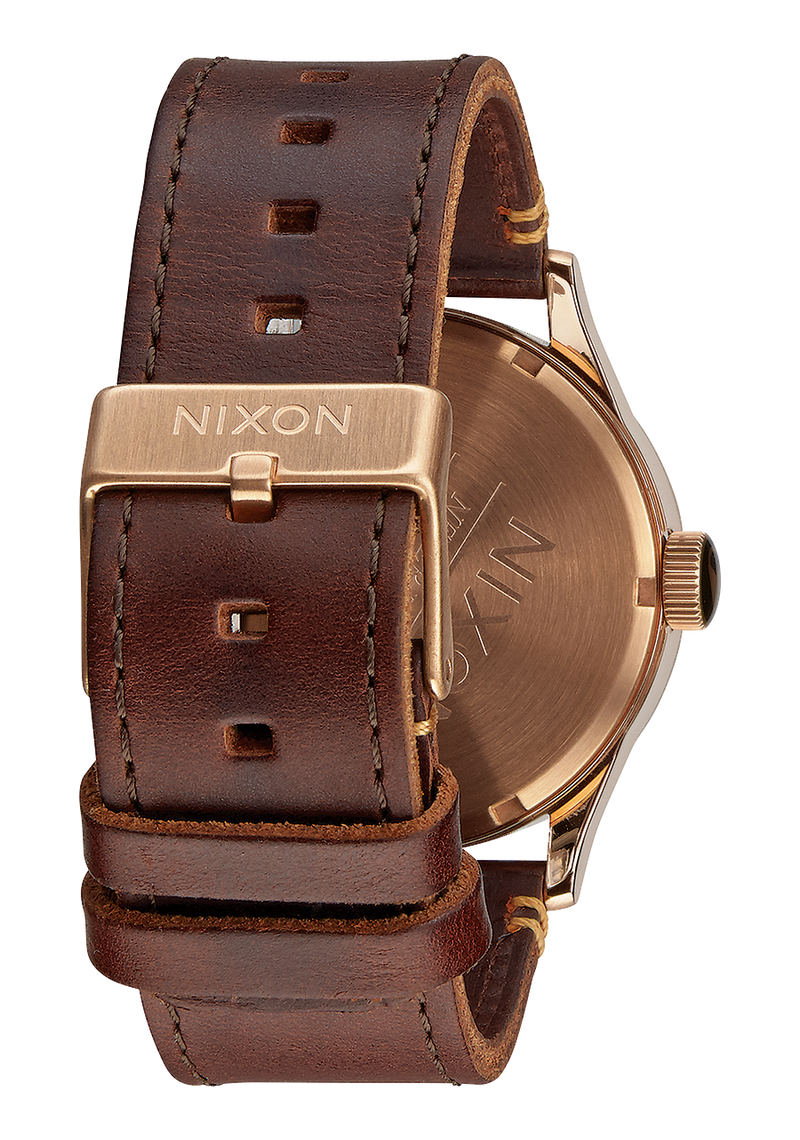 Wristwatch with a brown leather strap and gold-toned case bearing the Nixon brand name.