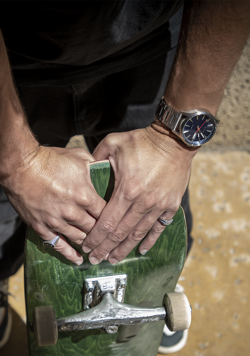 Green skateboard held by hands wearing a silver watch.