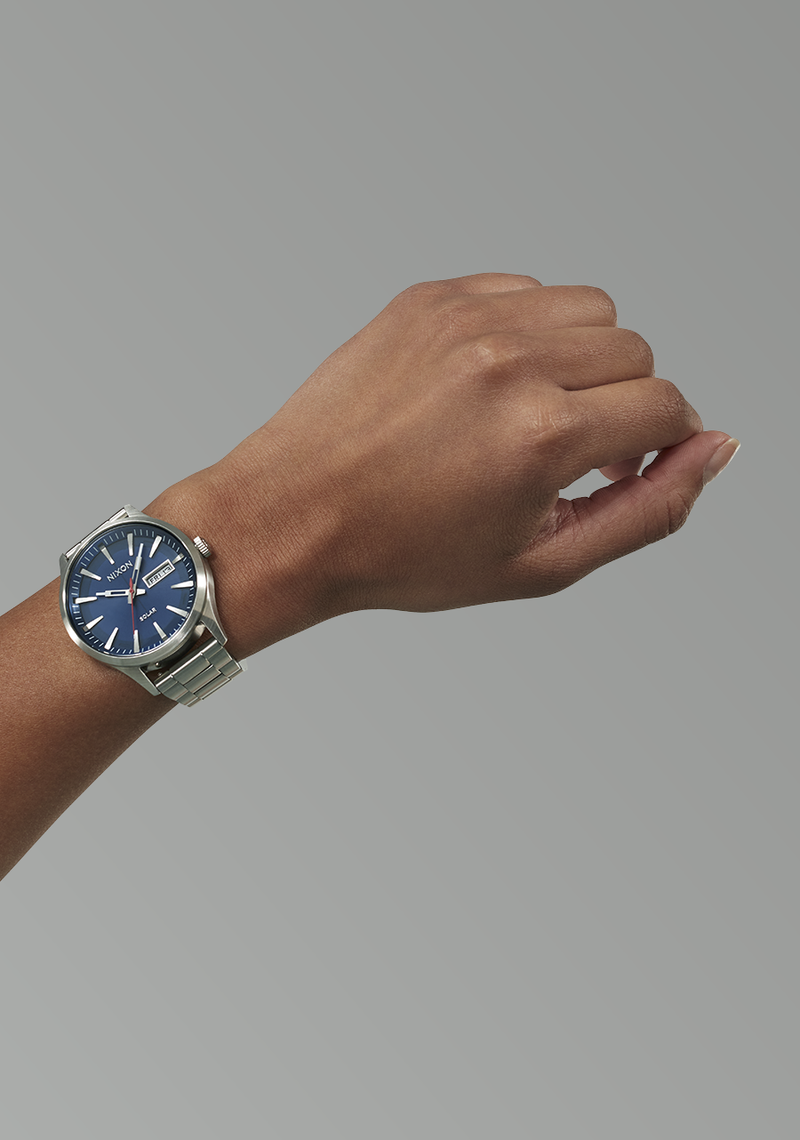 Wristwatch with a blue dial and silver metal bracelet worn on a person’s wrist.