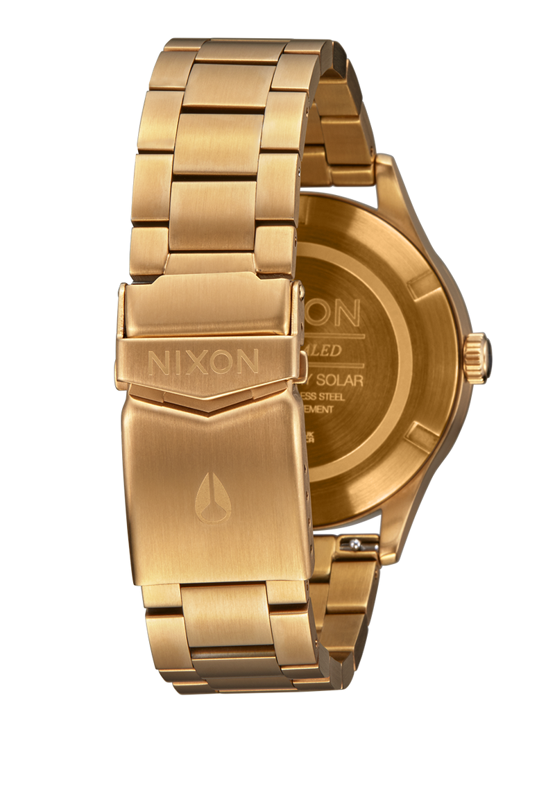 Gold-toned wristwatch with a metal bracelet and Nixon branding on the clasp and case back.