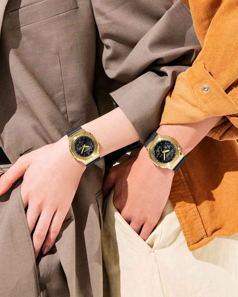 Two matching green and gold wristwatches worn side-by-side.