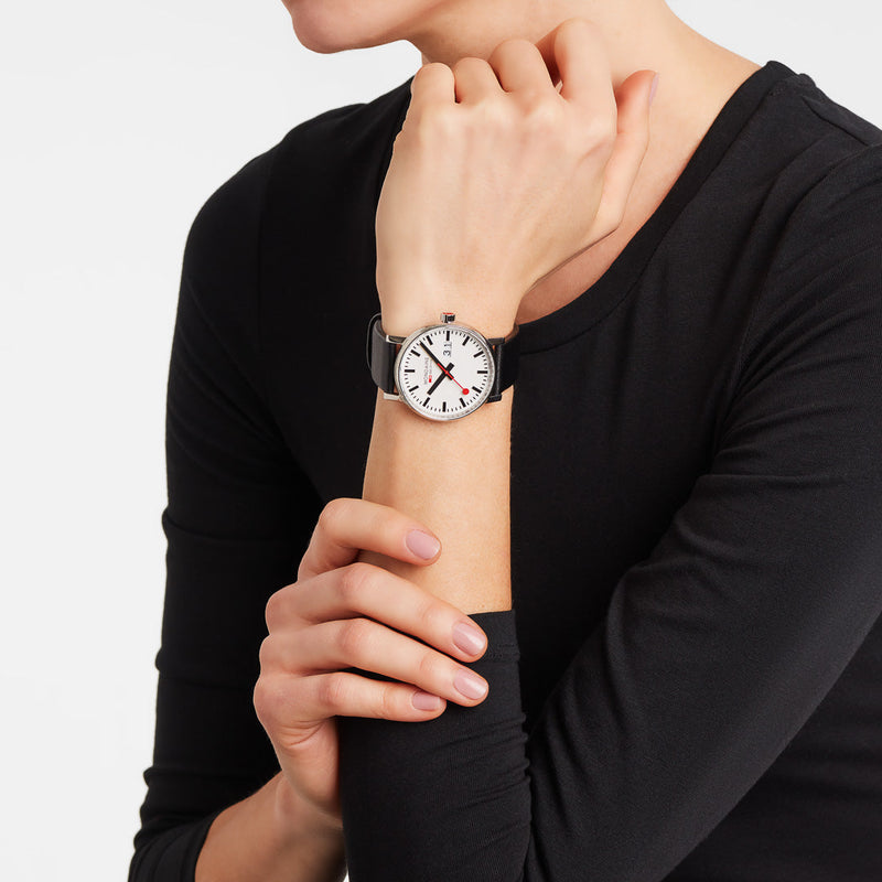 Wristwatch with a white face and black leather strap worn on a person’s wrist.