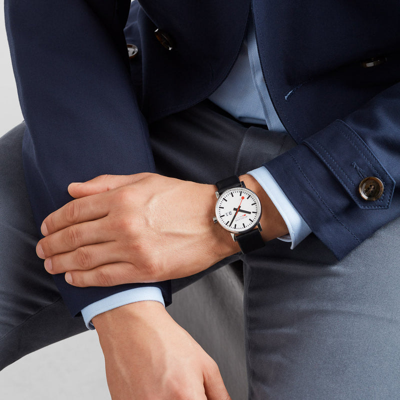 Wristwatch with a white face and black leather strap worn on a person’s wrist.