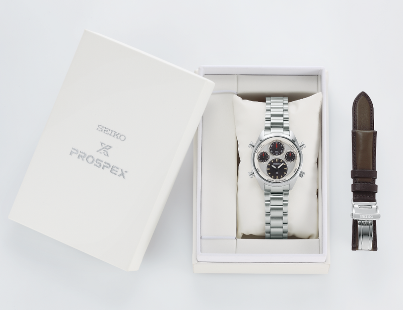 Luxury wristwatch with a silver metal band and multiple dials, presented in a white box alongside an additional leather strap.