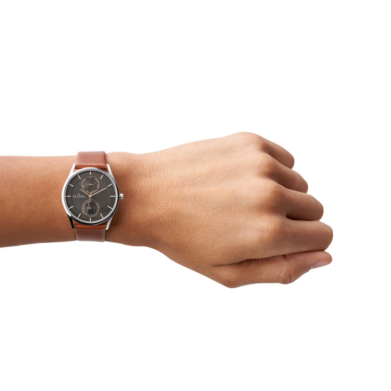 Wristwatch with a brown leather strap and dark face on a person’s wrist.