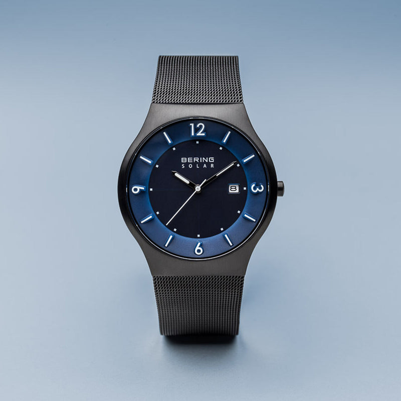 Sleek wristwatch with a dark mesh band and blue-accented circular face.