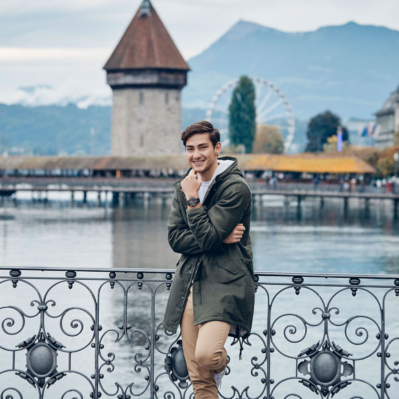 Young man in a green coat leaning against an ornate railing.