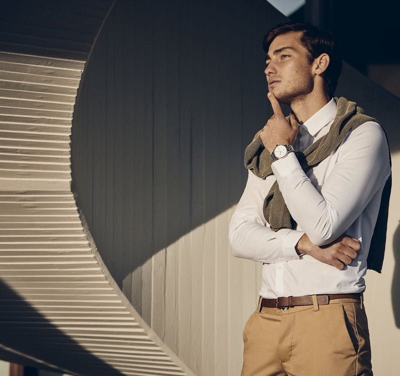 Young man in stylish casual attire posing against a wall.