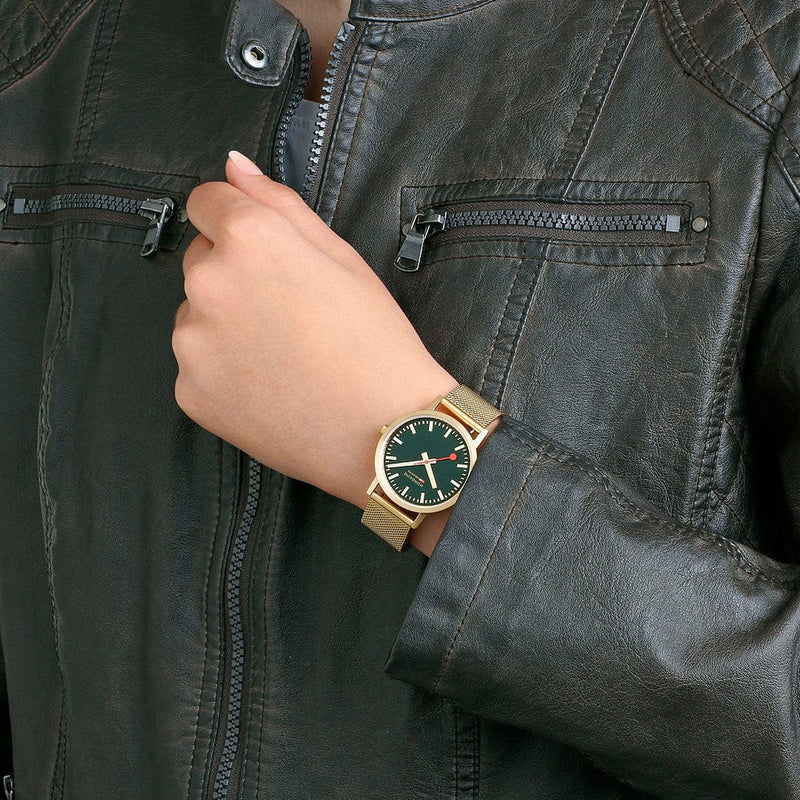 Gold wristwatch with a green dial worn on a person’s wrist.