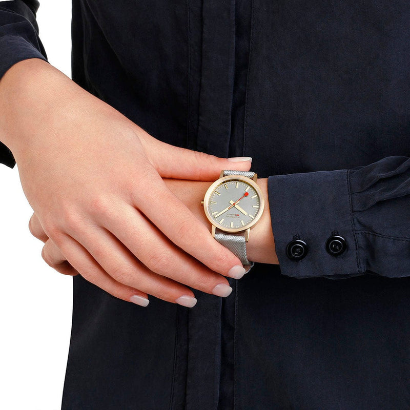 Gold-toned wristwatch with a light-colored leather strap worn on a person’s wrist.