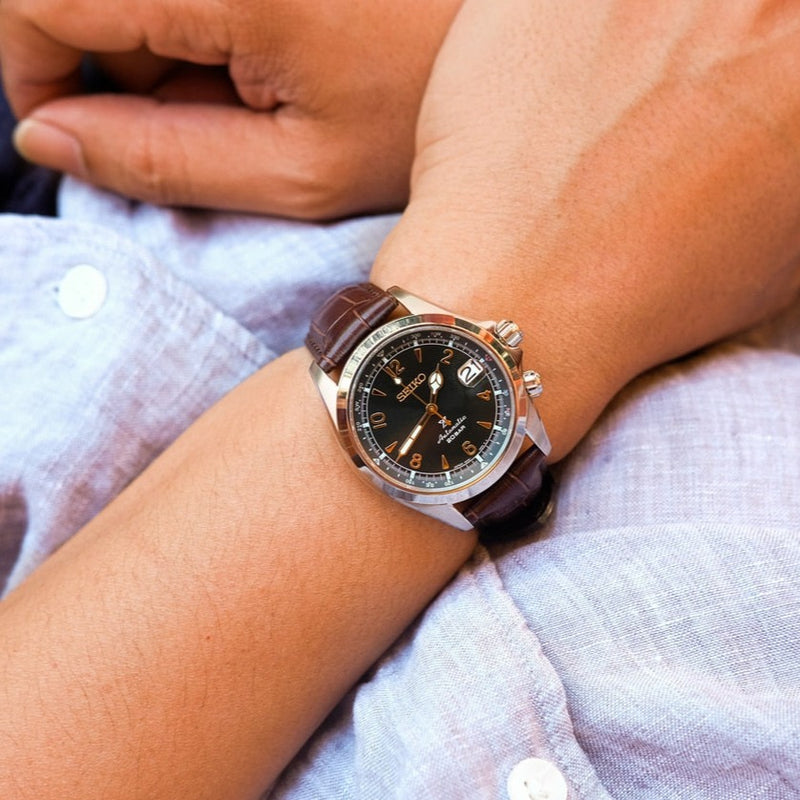 Wristwatch with a brown leather strap and black dial face.