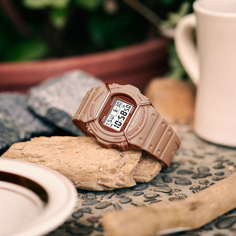 Rose gold digital wristwatch with a rectangular display resting on a piece of driftwood.