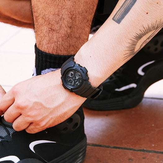 Black digital wristwatch with multiple dials worn on a tattooed arm.