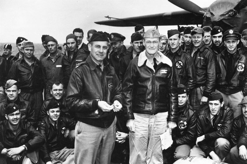 Group of military aviators or pilots posing together in front of an aircraft.