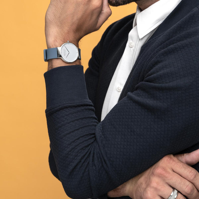 Wristwatch with a minimalist design on a person’s arm wearing a dark suit jacket.